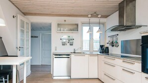 Moderni keittiö, jossa on valkoiset kaapit, astianpesukone ja ruostumattomasta teräksestä valmistettu liesituuletin. Keittiössä on ikkuna, josta tulee luonnonvaloa, ja ovi, joka johtaa toiseen huoneeseen.