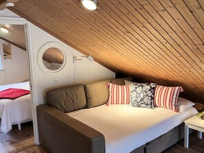 A cozy attic bedroom with a wooden sloped ceiling, a round window, and a bed with multiple pillows.