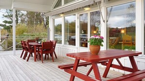 A covered outdoor deck with wooden furniture, including a table and chairs, and a flower pot. - Holiday Home in Brastad (Brastad)
