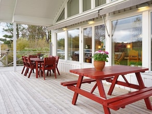 A covered outdoor deck with wooden furniture, including a table and chairs, and a flower pot. - Holiday Home in Brastad (Brastad)