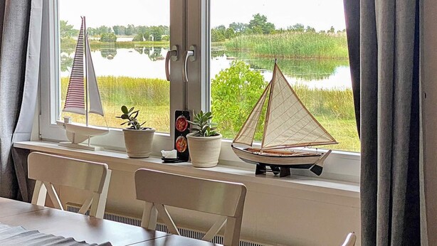 Ein Essbereich mit Seeblick, zwei Segelboote auf der Fensterbank und ein Blumentopf.