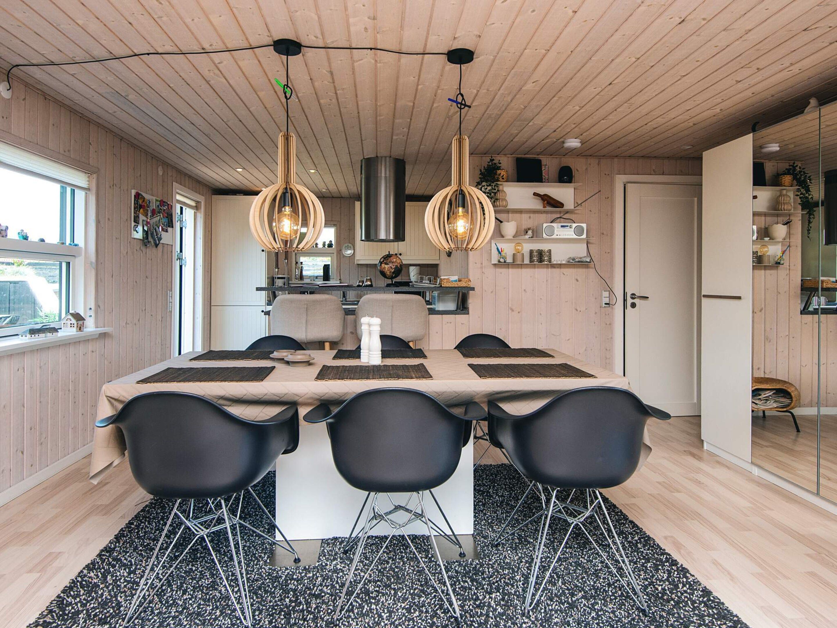 A modern kitchen with wooden paneling, a dining area with a large table and black chairs, and pendant lighting.