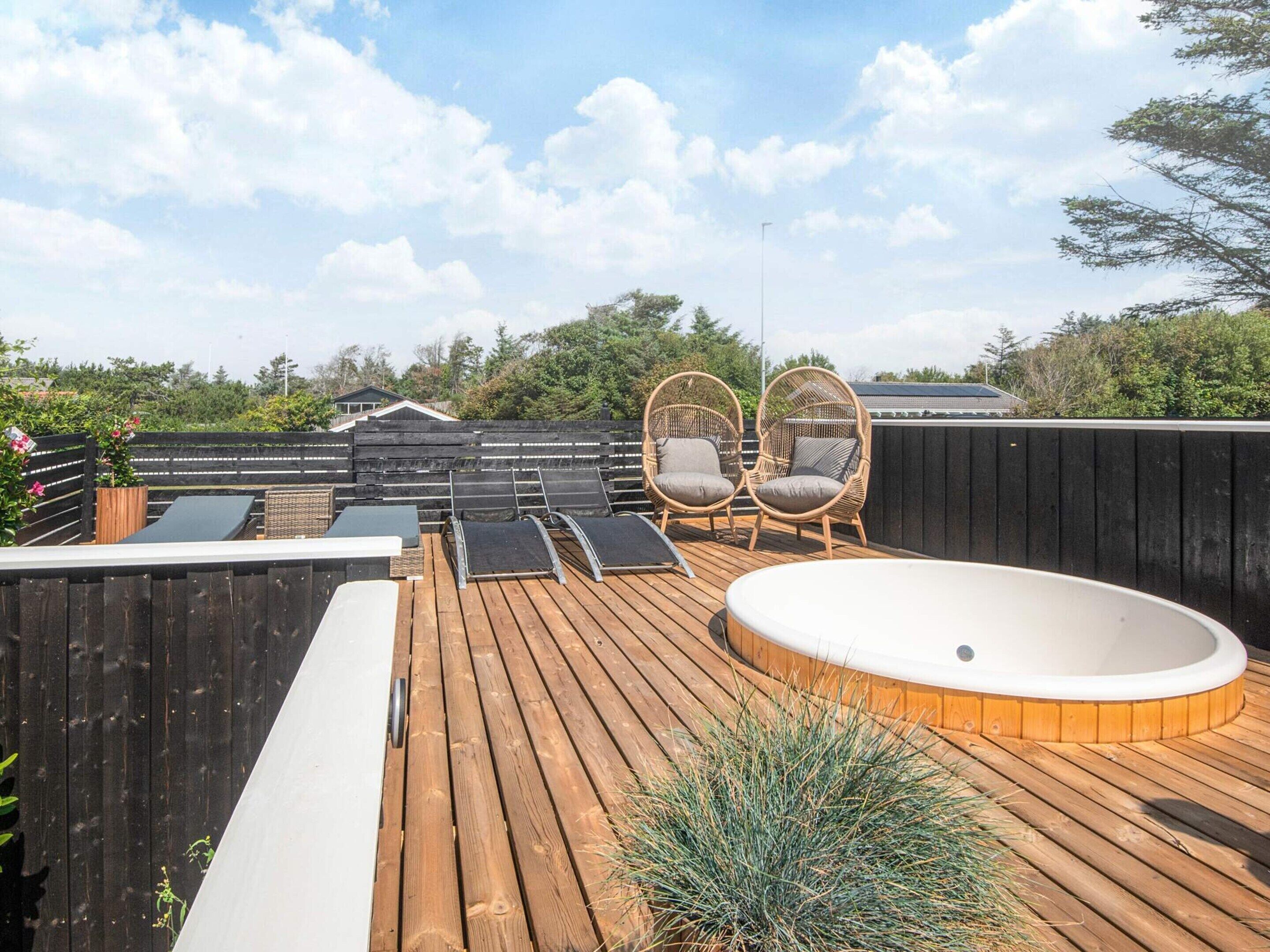 A wooden deck with a hot tub, two wicker chairs, and a small table.