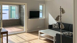 A modern living room with a television on a shelf, a sofa with patterned cushions, a coffee table, and a floor lamp. - Holiday Home in Dyrvik (Frøya)