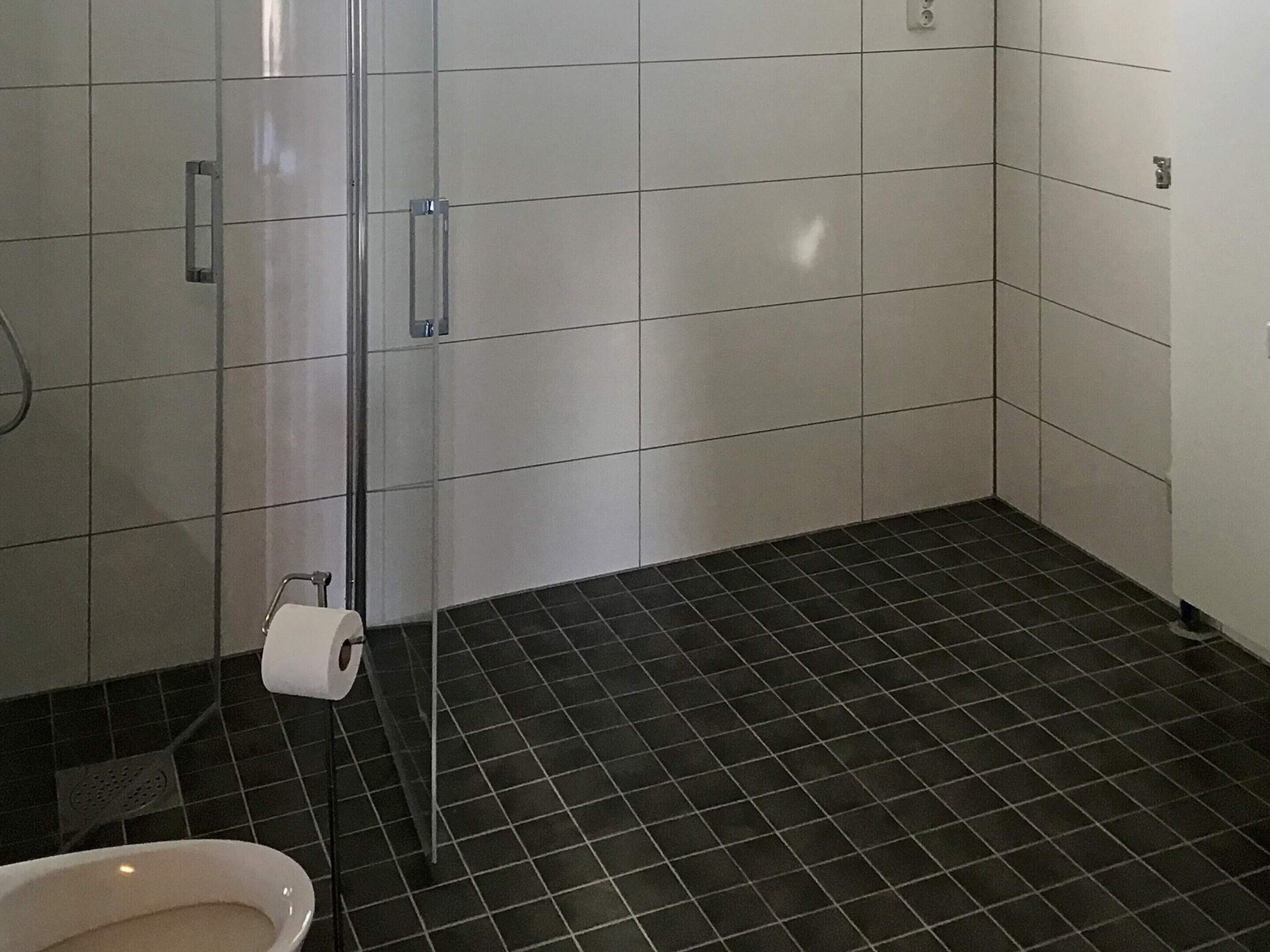 Un baño con inodoro, cabina de ducha y suelo de baldosas.