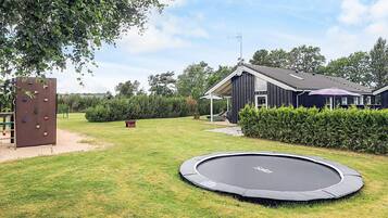 En baghave med trampolin, klatrevæg, hus og velplejet græsplæne.