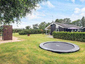 A backyard with a trampoline, a climbing wall, a house, and a well-maintained lawn.