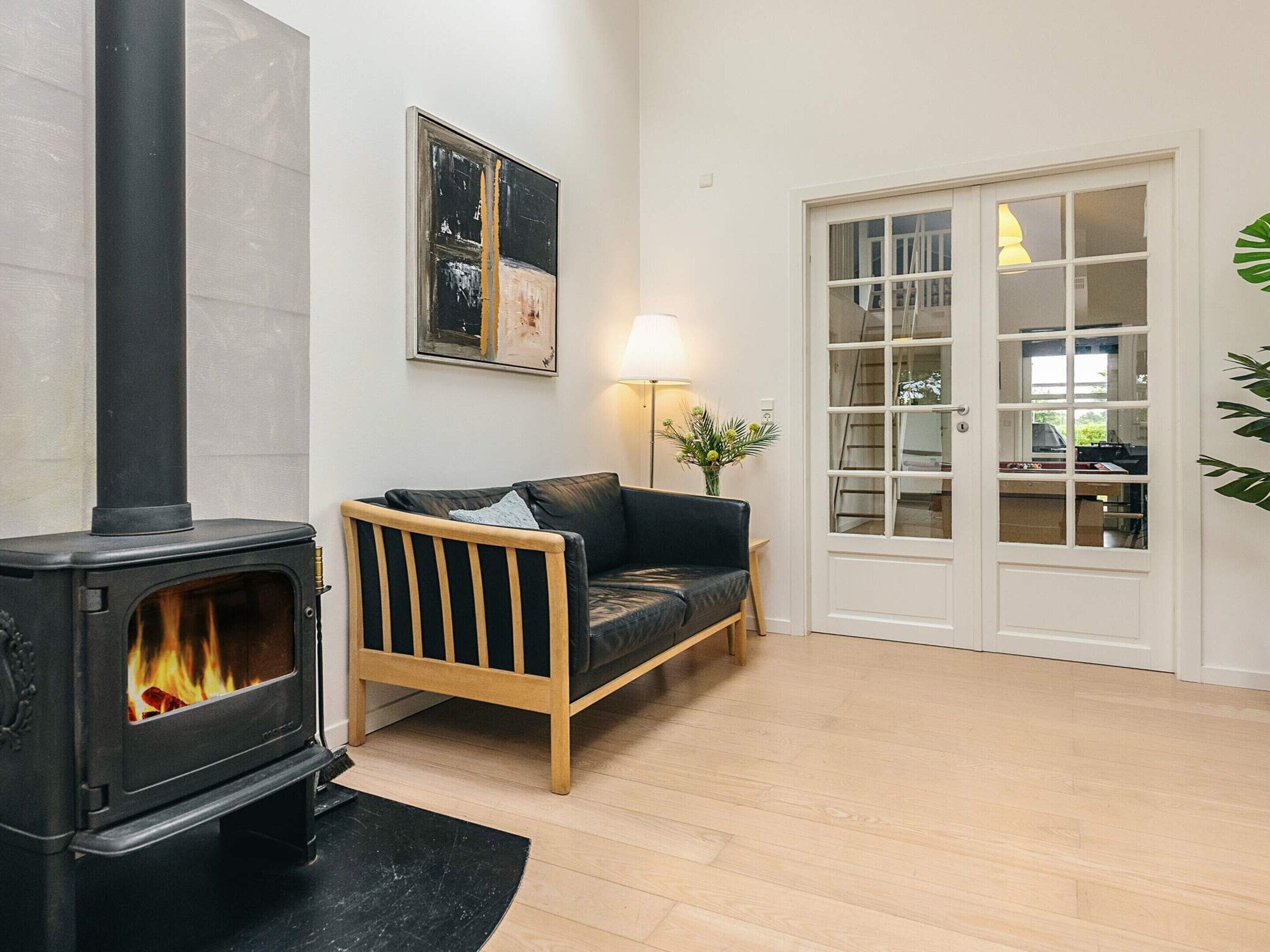 A cozy living room with a black wood-burning stove, a wooden sofa, a white door with glass panels, and a framed abstract painting on the wall.
