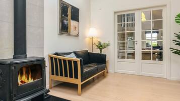 A cozy living room with a black wood-burning stove, a wooden sofa, a white door with glass panels, and a framed abstract painting on the wall.