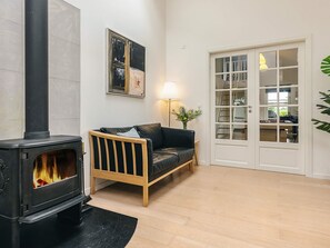 Ein gemütliches Wohnzimmer mit einem schwarzen Kaminofen, einem Holzsofa, einer weißen Tür mit Glasscheiben und einem gerahmten abstrakten Gemälde an der Wand.