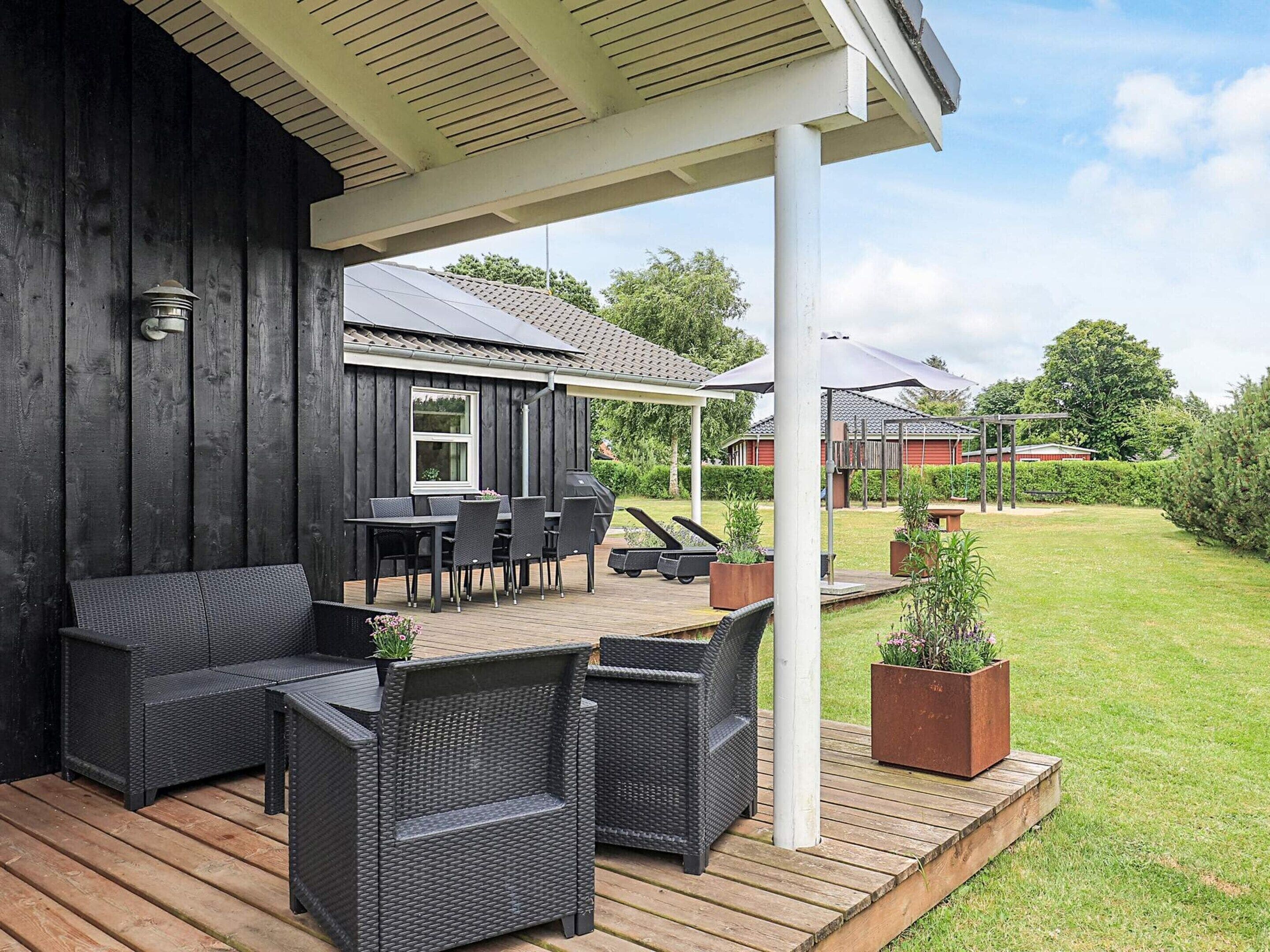 A covered patio area with outdoor furniture, a grill, and a view of a house in the background.