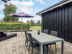En udendørs terrasse med et bord og stole, en lilla parasol og et sort hegn i baggrunden.