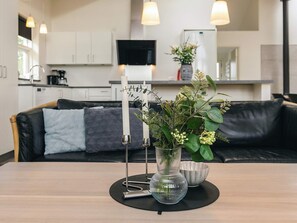 Et moderne køkken med hvide skabe, en sort bordplade og en lædersofa i sort i baggrunden.