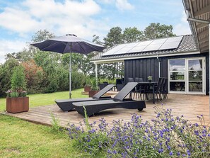 A patio with outdoor furniture, a pergola, and a garden with blue flowers.