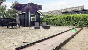 Ein Garten mit einem Shuffleboardtisch, einem Terrassentisch mit Stühlen und einem dunklen Holzschuppen.