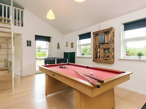 A pool table with cues and balls, a foosball table, and a lofted seating area.