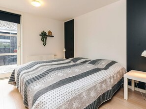 Et soveværelse med en stor seng, et lille natbord, en radiator, et vindue med udsigt og en plante på væggen.