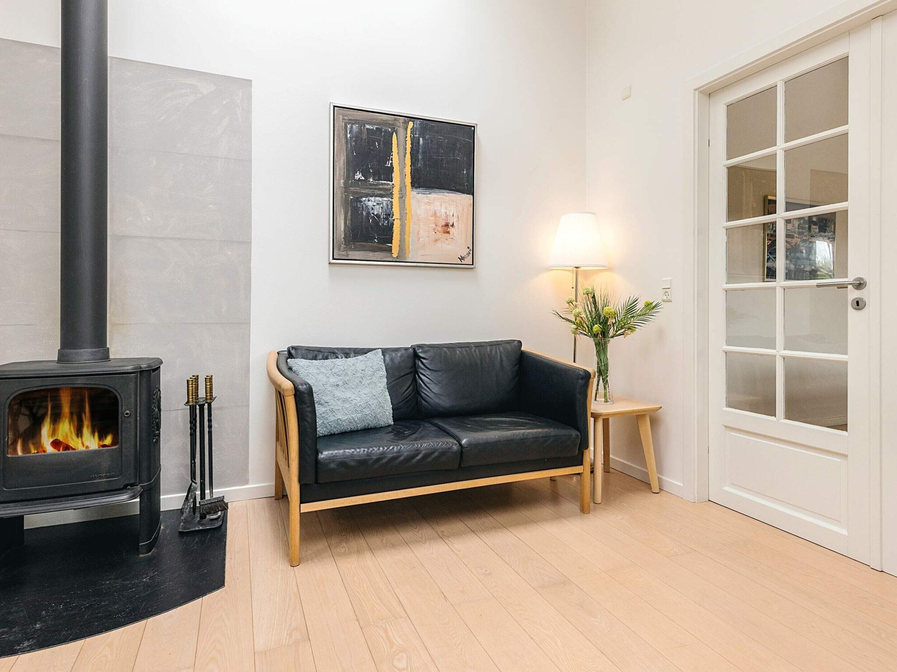 Un salon avec un canapé en cuir noir, une porte blanche, une cheminée et un tableau abstrait encadré accroché au mur.