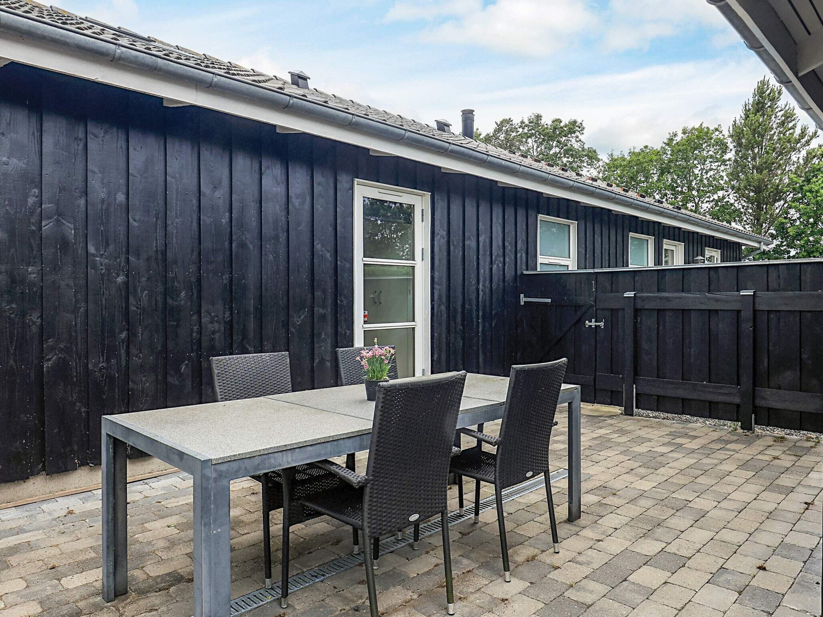 Un patio con tavolo e sedie, una recinzione nera e una casa con finestra e porta.