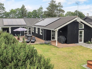 Moderni talo, jossa on katettu terassi, grillauspaikka ja aurinkopaneeleilla varustettu katto.