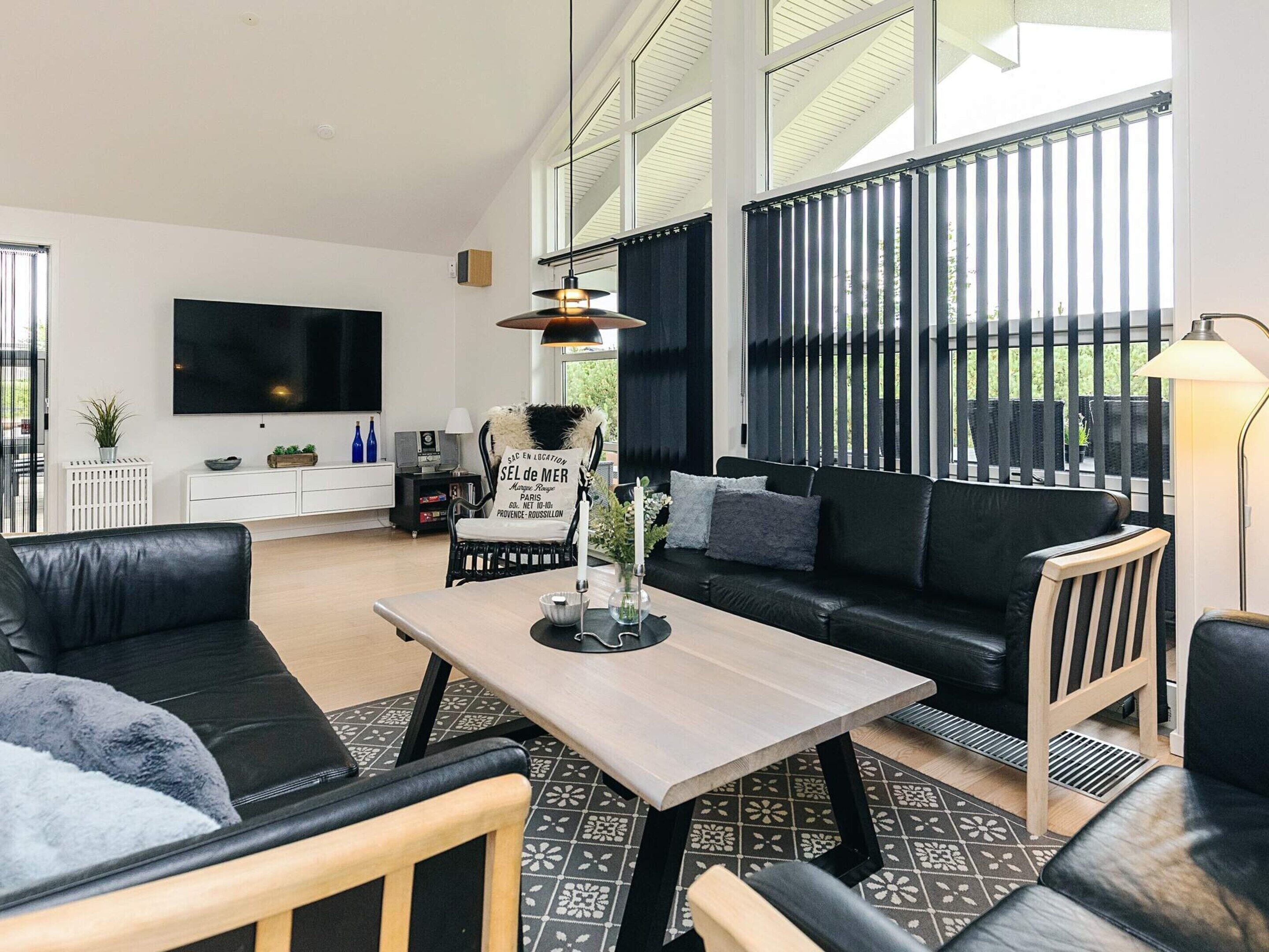 A modern living room with a black leather sofa, a wooden coffee table, and a TV mounted on the wall.