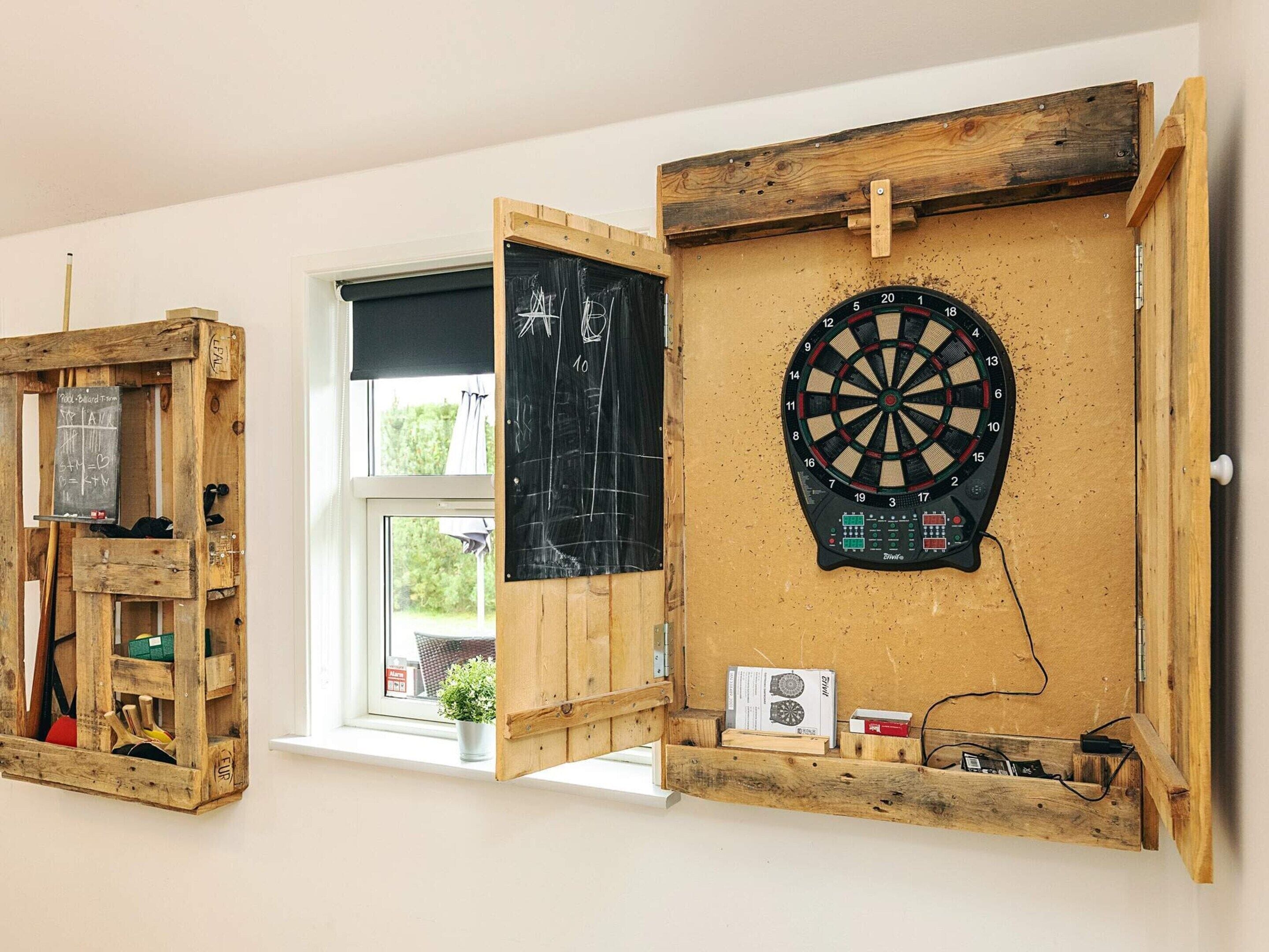 A room with a dartboard, a chalkboard, and a wooden shelf unit.