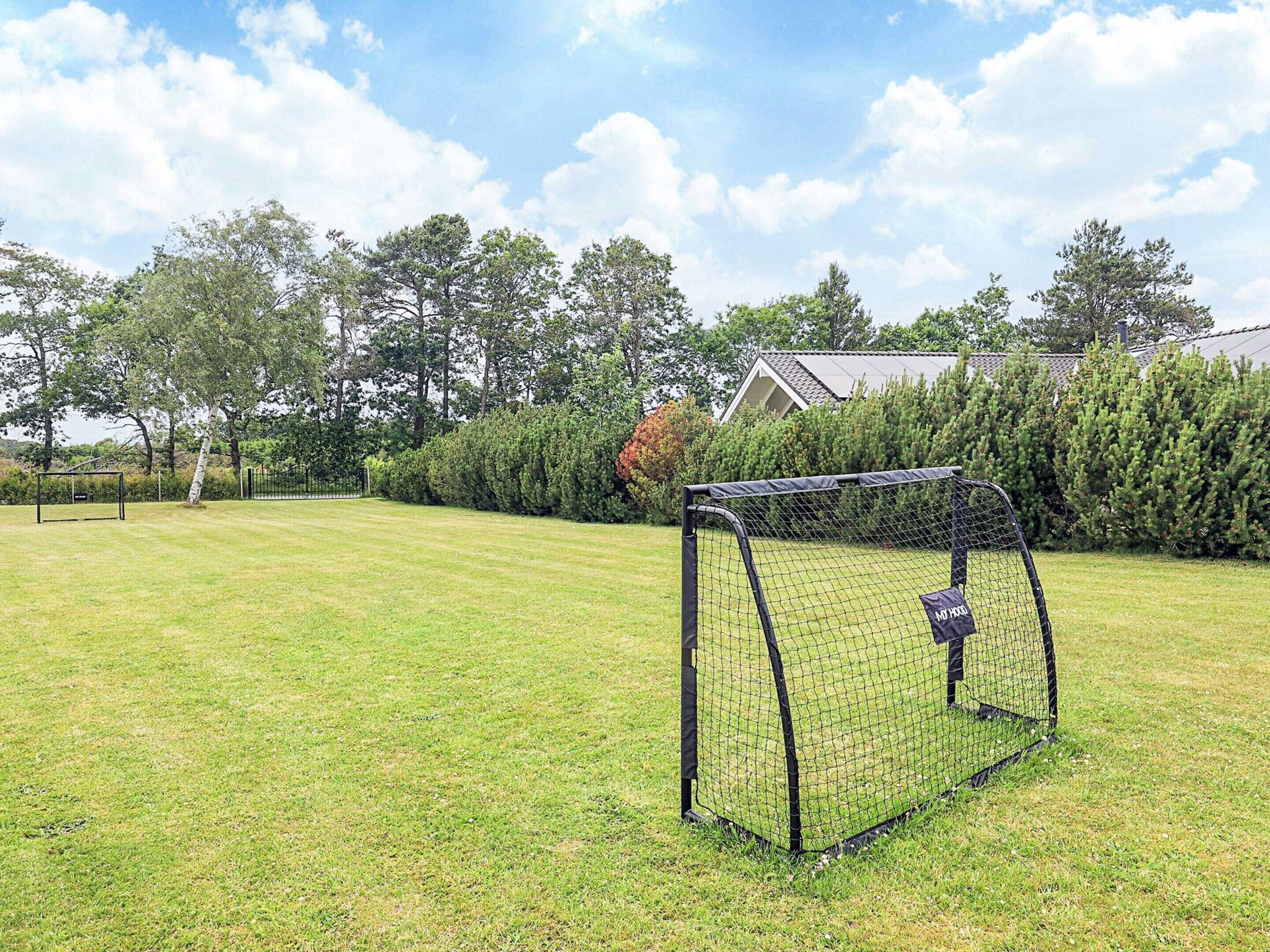 A soccer goal in a grassy field with a house and trees in the background.