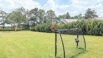 A soccer goal in a grassy field with a house and trees in the background.
