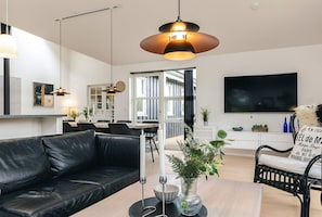 Una sala de estar moderna con un sofá de cuero negro, un comedor con una mesa blanca y un televisor grande en la pared.
