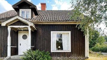 Ett trähus med ett sadeltak, en skorsten, en ytterdörr och ett fönster.