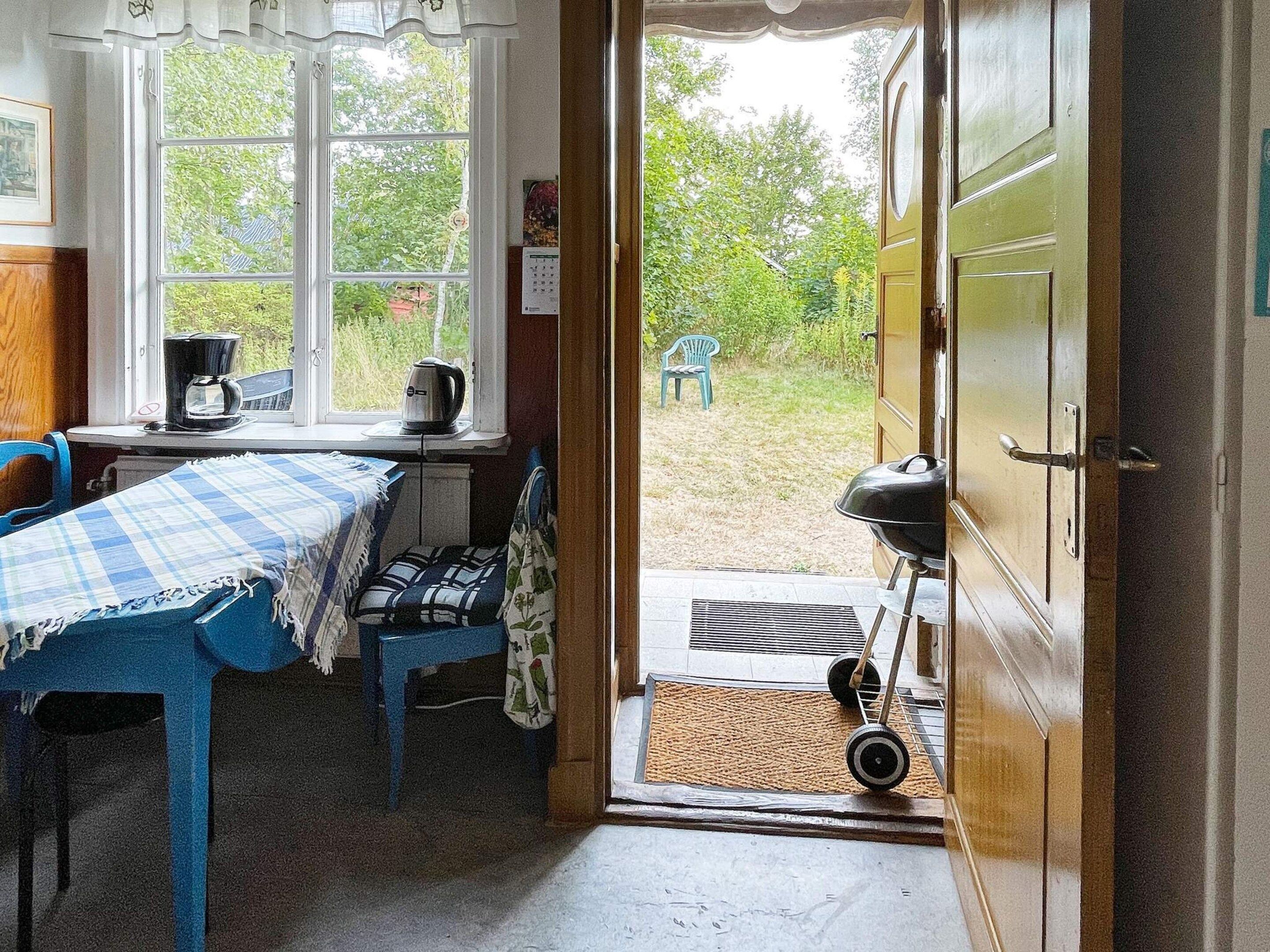 A room with a table and chairs, a window with a view of greenery, and a door leading outside.