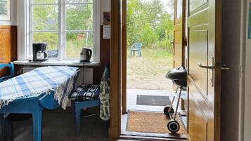 A room with a table and chairs, a window with a view of greenery, and a door leading outside.
