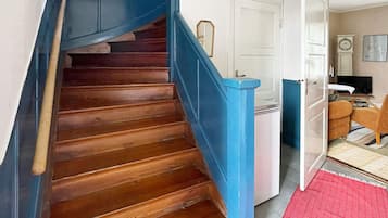A wooden staircase with blue handrails leading to a room with a white door, a clock, and a television.