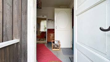 Un pasillo con puerta de madera, alfombra roja y un pequeño cofre de madera.
