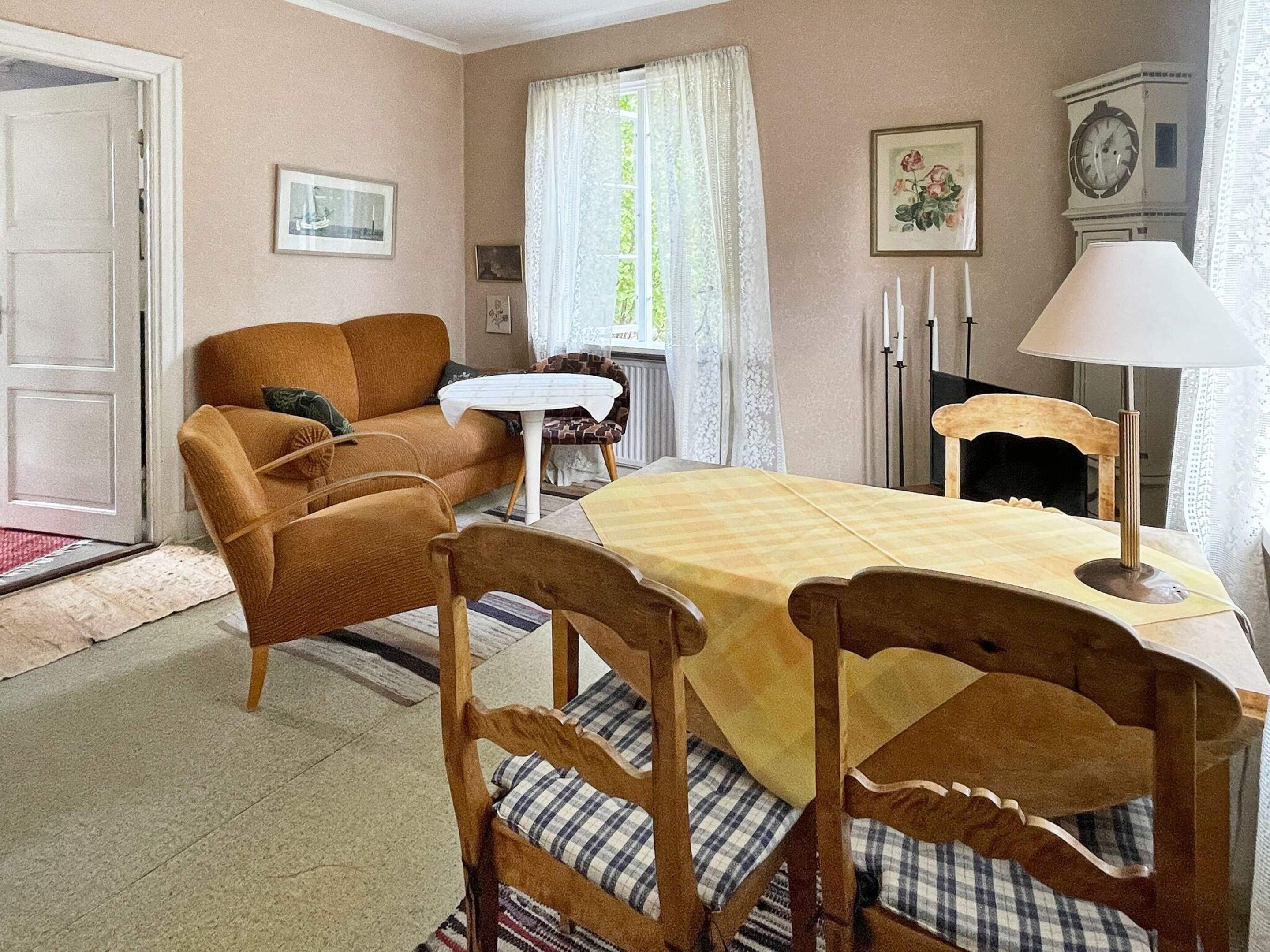 Ein gemütliches Wohnzimmer mit einer Couch, einem Esstisch mit Stühlen, einem kleinen Beistelltisch und einer Wanduhr.