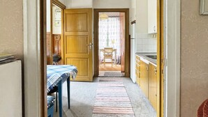 A narrow hallway with a dining table and chairs, a kitchen area with cabinets, and a view into a dining room with a table and chairs. - 5 Person Holiday Home in Linneryd/kronobergs Lan (Linneryd)