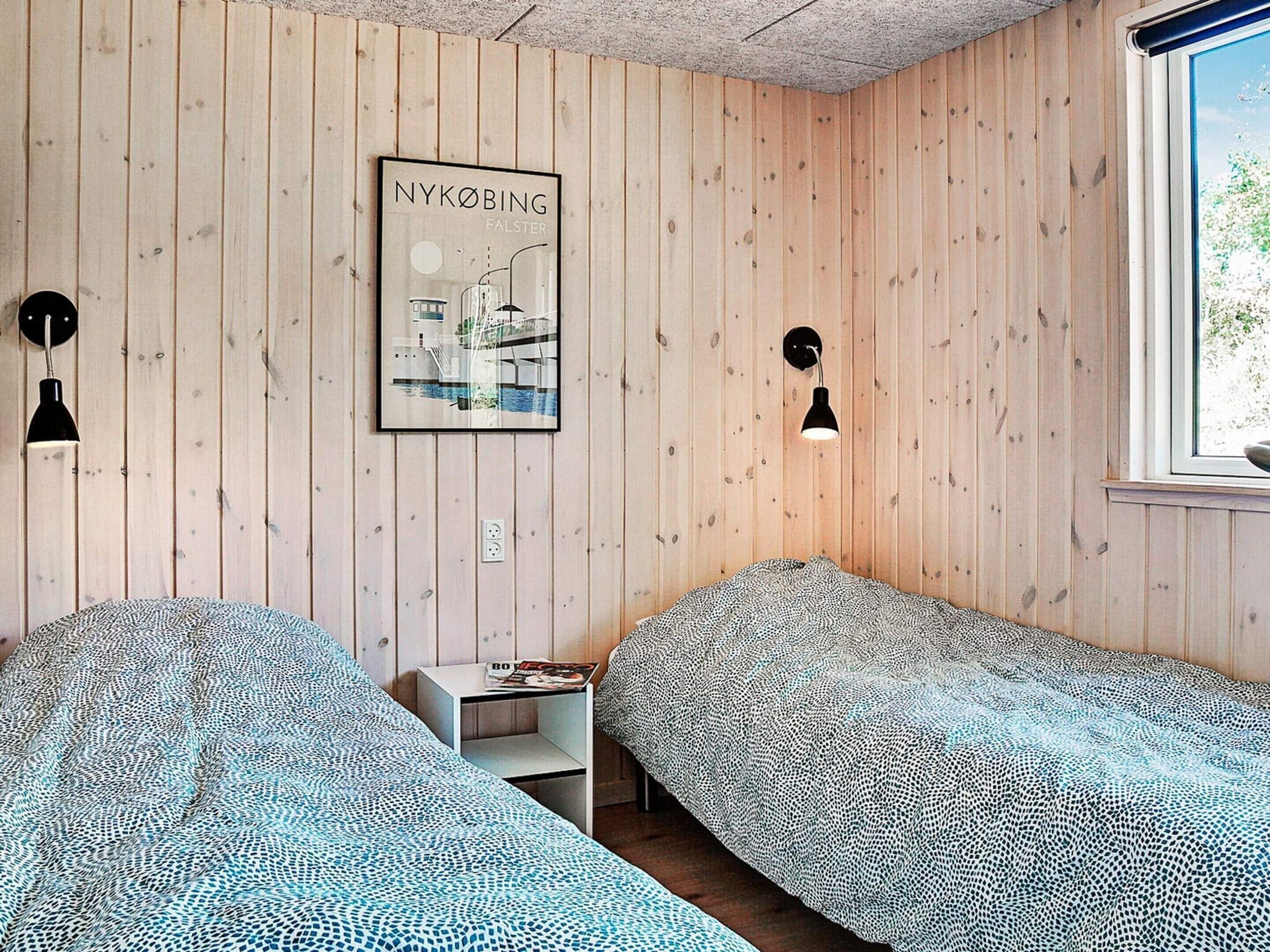 A room with two beds, wooden walls, a framed picture, and a window.