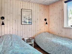 Une chambre avec deux lits, des murs en bois, un tableau encadré et une fenêtre.