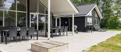A covered outdoor seating area with tables and chairs, a wooden bench, and a grill.