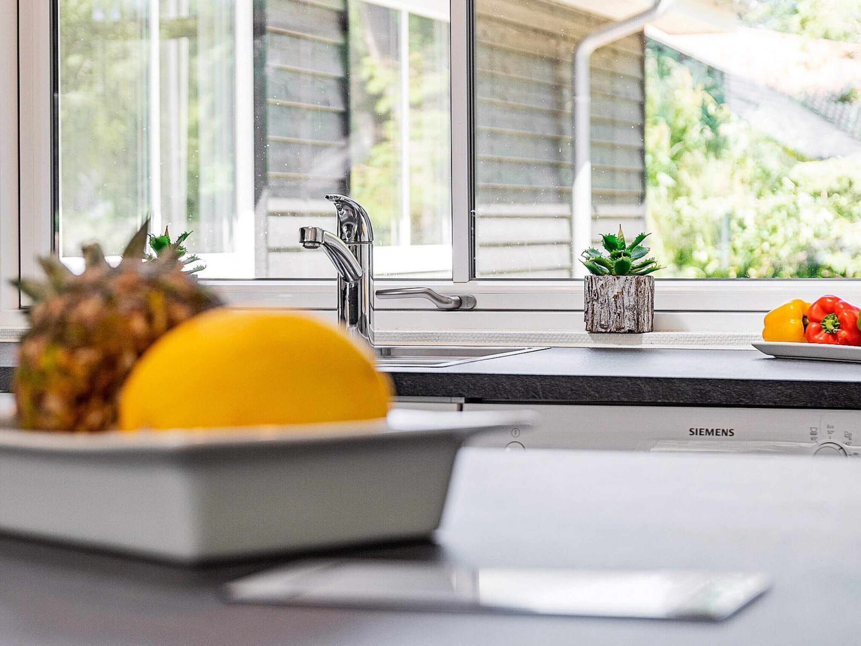 A kitchen with a Siemens dishwasher, a window with blinds, and a fruit bowl with pineapple and lemon.