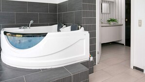 A modern bathroom with a freestanding bathtub, dark tiled walls, and a white sink area.