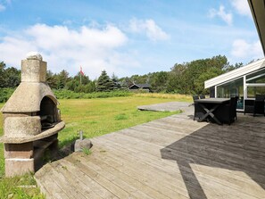 An outdoor area with a stone-built oven, a wooden deck, and a glass-enclosed structure.
