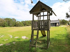 A wooden play structure with a slide in a grassy field.