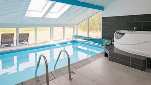 An indoor swimming pool with clear glass walls, a sunroof, and a spa area.