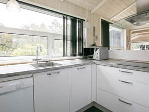 A modern kitchen with white cabinetry, a built-in dishwasher, and a window providing a view of trees.
