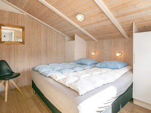 A bedroom with a wooden ceiling, a bed with white and blue bedding, a chair, and two wall-mounted lamps. - Holiday Home in Løkken (Lokken)