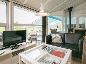 A living room with a television, a glass coffee table, a sofa, and a fireplace. - Holiday Home in Løkken (Lokken)