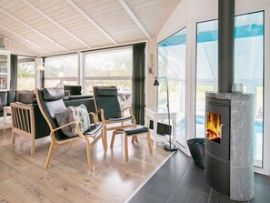 A modern living room with a stone fireplace, wooden flooring, and large windows offering a view of the outdoors.
