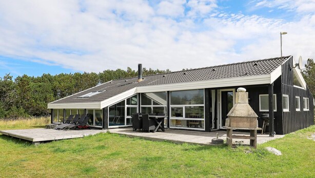 A modern house with a large patio, outdoor seating, and a stone fireplace.