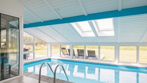 An indoor swimming pool with clear glass walls, a tiled floor, and a blue ceiling.